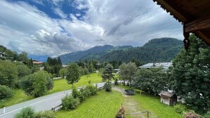 Uitzicht vanaf een balkon op een groen landschap met een weg, bomen en bergen in de verte.