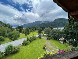 Blick von einem Balkon auf eine grüne Landschaft mit einer Straße, Bäumen und Bergen in der Ferne.