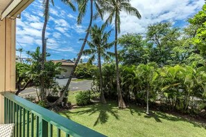 A balcony with a view of a road, palm trees, and a building. - Kalama Terrace L203 2 Bedroom Apts (Kihei)