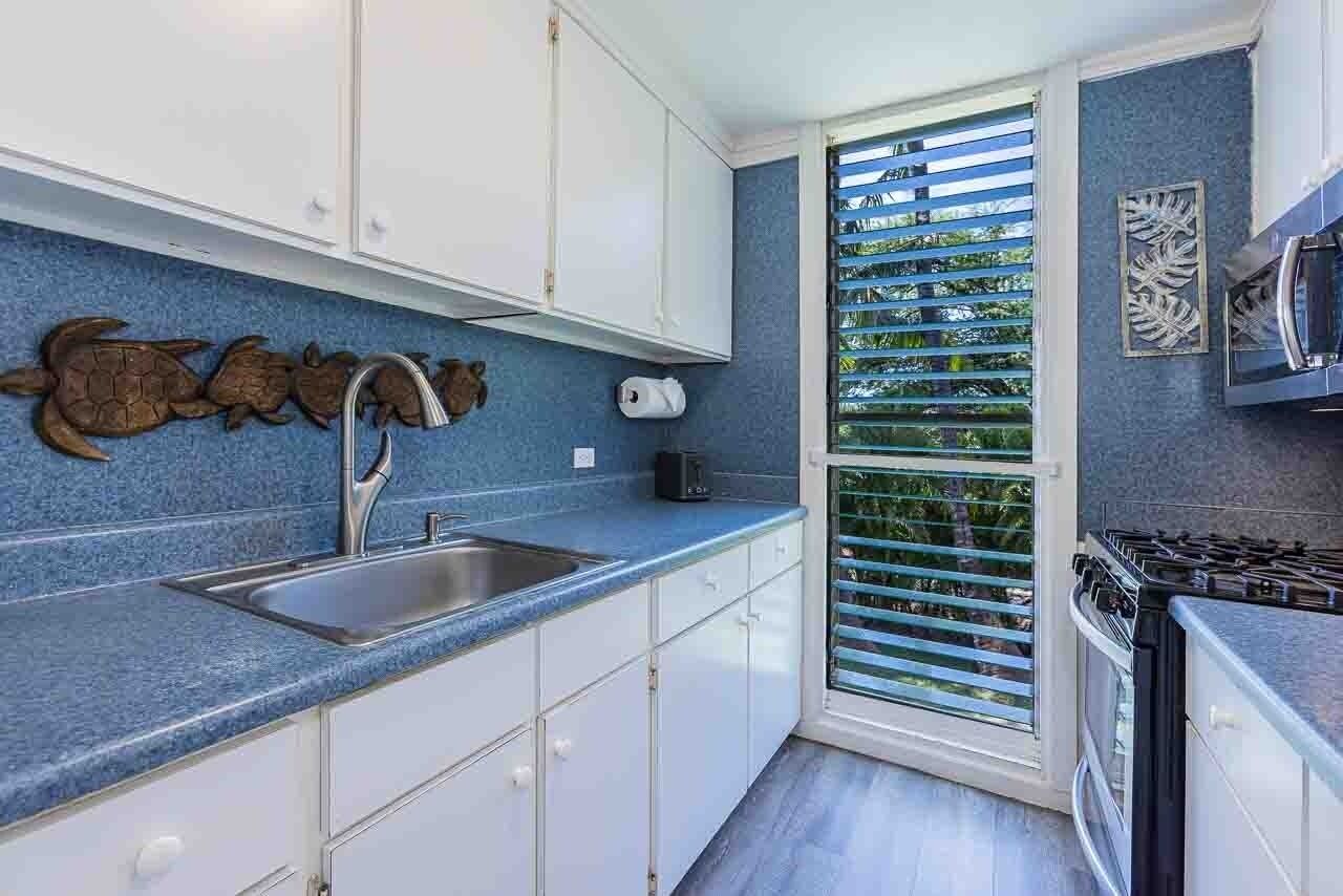 A kitchen with a blue countertop, white cabinets, a stainless steel sink, and a stove.