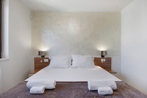 A hotel room with a large bed, two bedside lamps, and two rolled towels on the bed.