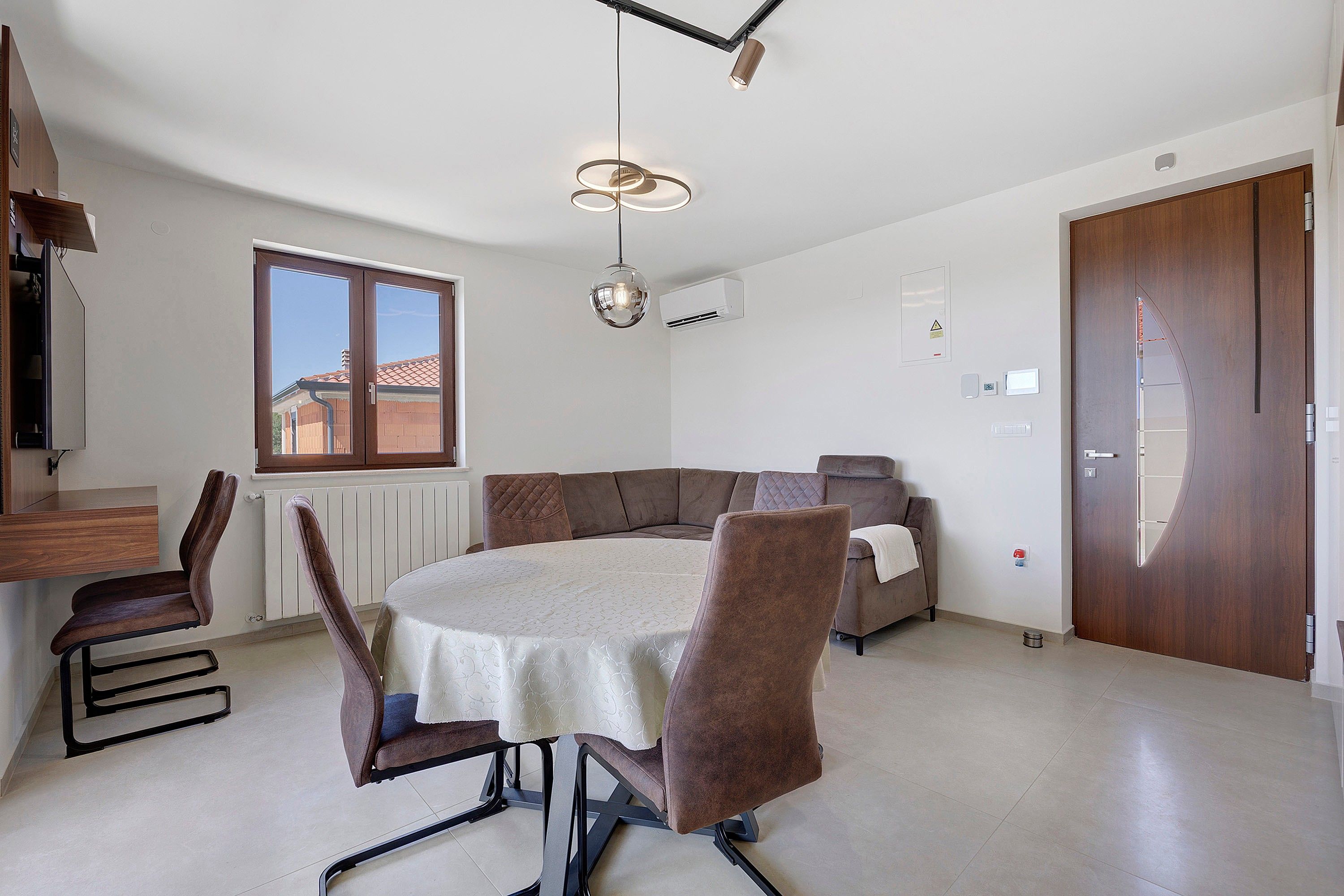 A modern living room with a dining table, chairs, a sofa, and a large window.