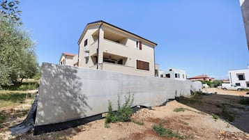 A multi-story residential building with a balcony, a concrete retaining wall, and a dirt ground with sparse vegetation.