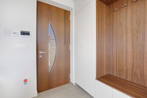 Un pasillo con una puerta de madera, una pared blanca con un termostato y un armario de madera.