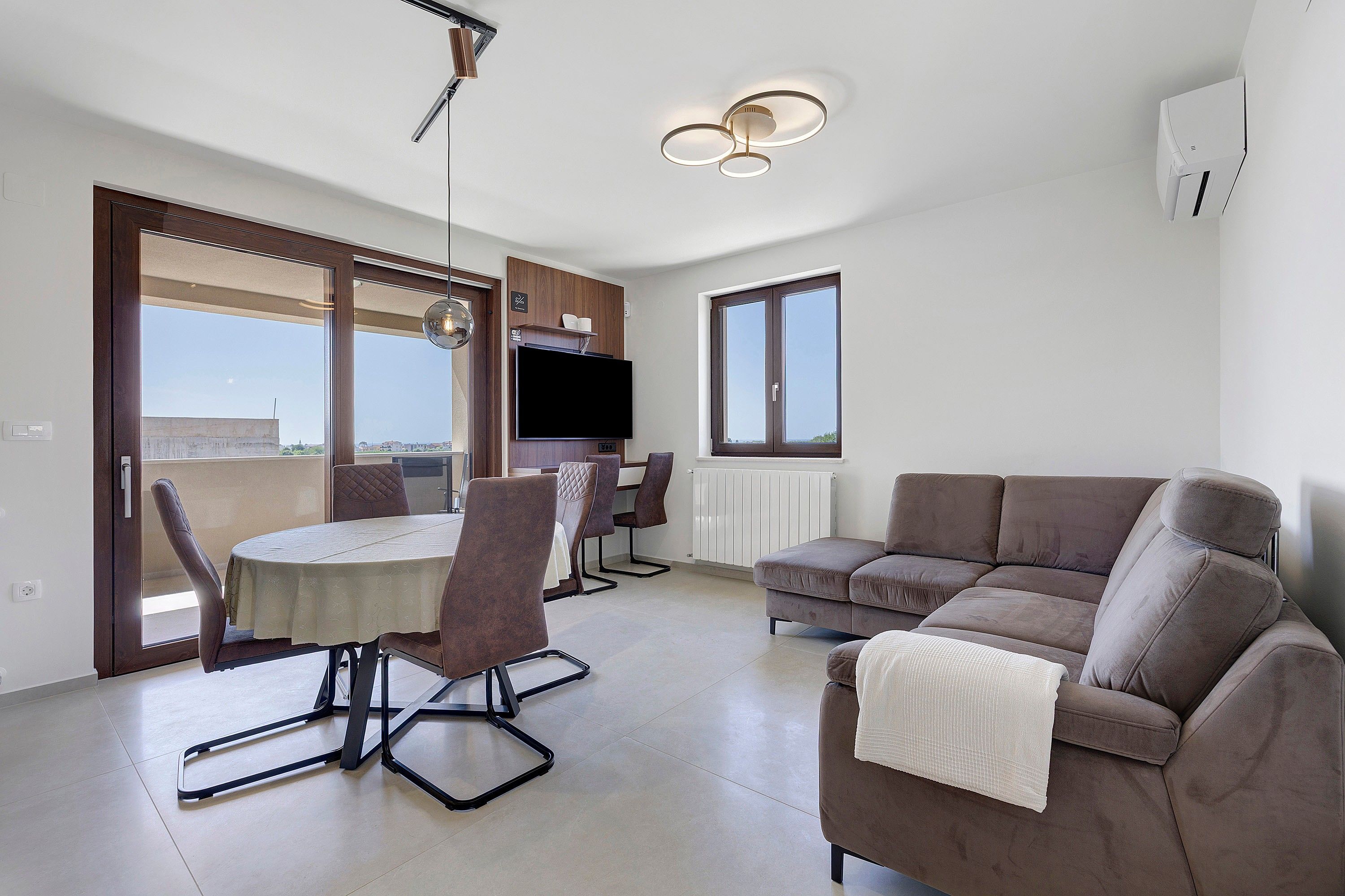 Un apartament modern amb zona de menjador, sofà, televisió i vistes per les finestres.