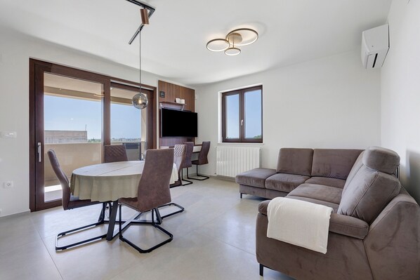 Un appartement moderne doté d’un coin repas, d’un canapé, d’une télévision et offrant une vue par les fenêtres.
