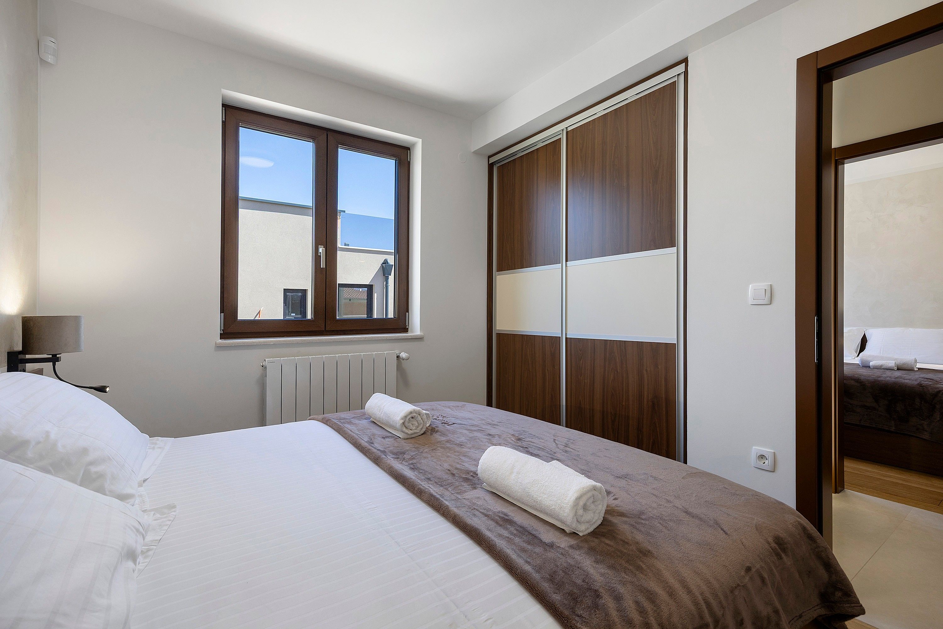 A hotel room with a bed, a window, a radiator, and a wardrobe.