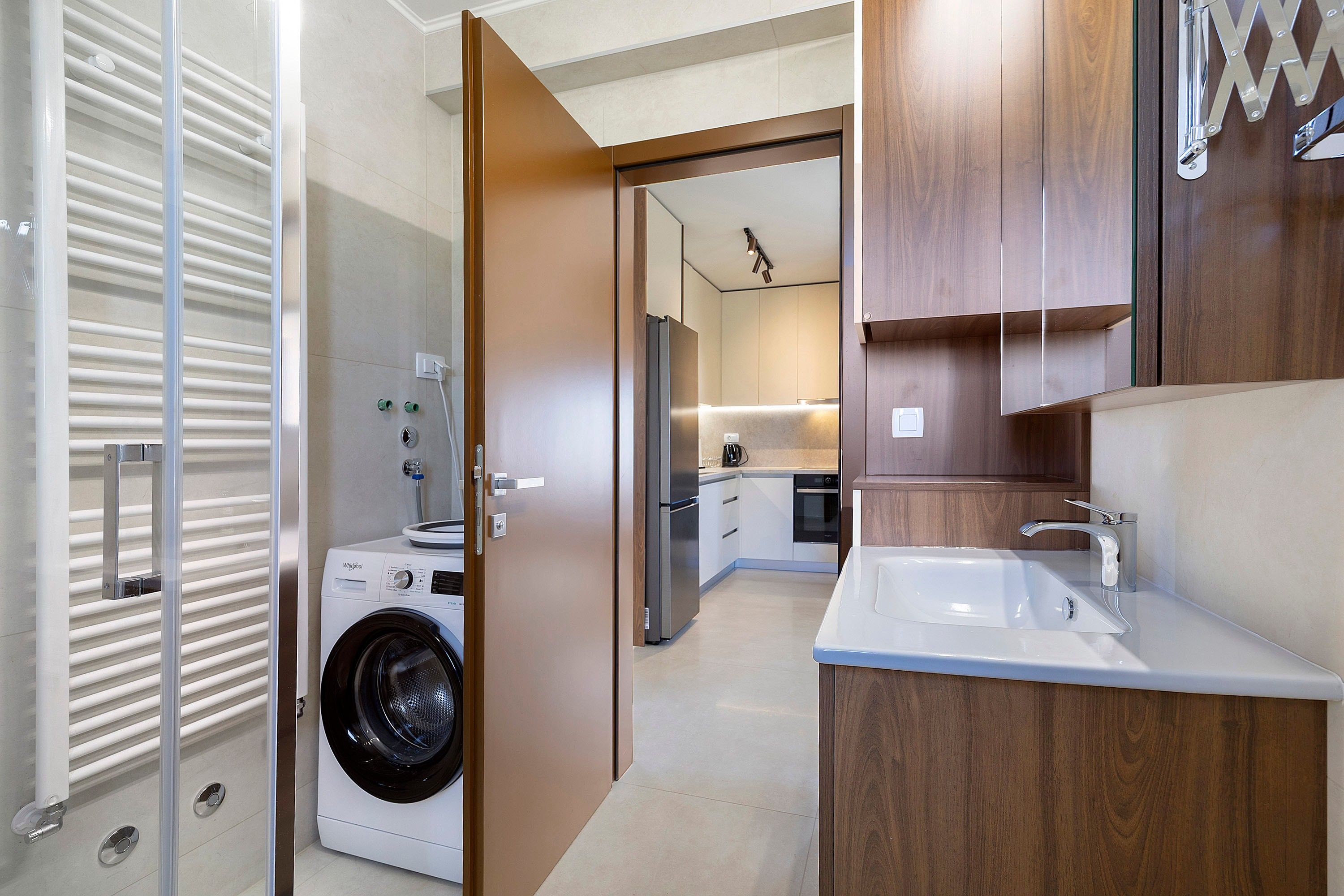 Une salle de bain moderne équipée d’un lave-linge intégré, d’un évier et de meubles de rangement en bois.