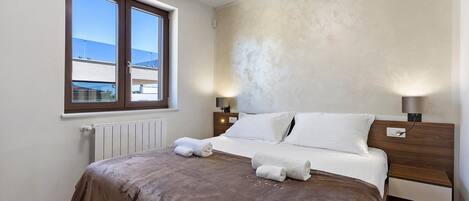 Un dormitorio con una cama, dos lámparas de noche, una ventana y un radiador.