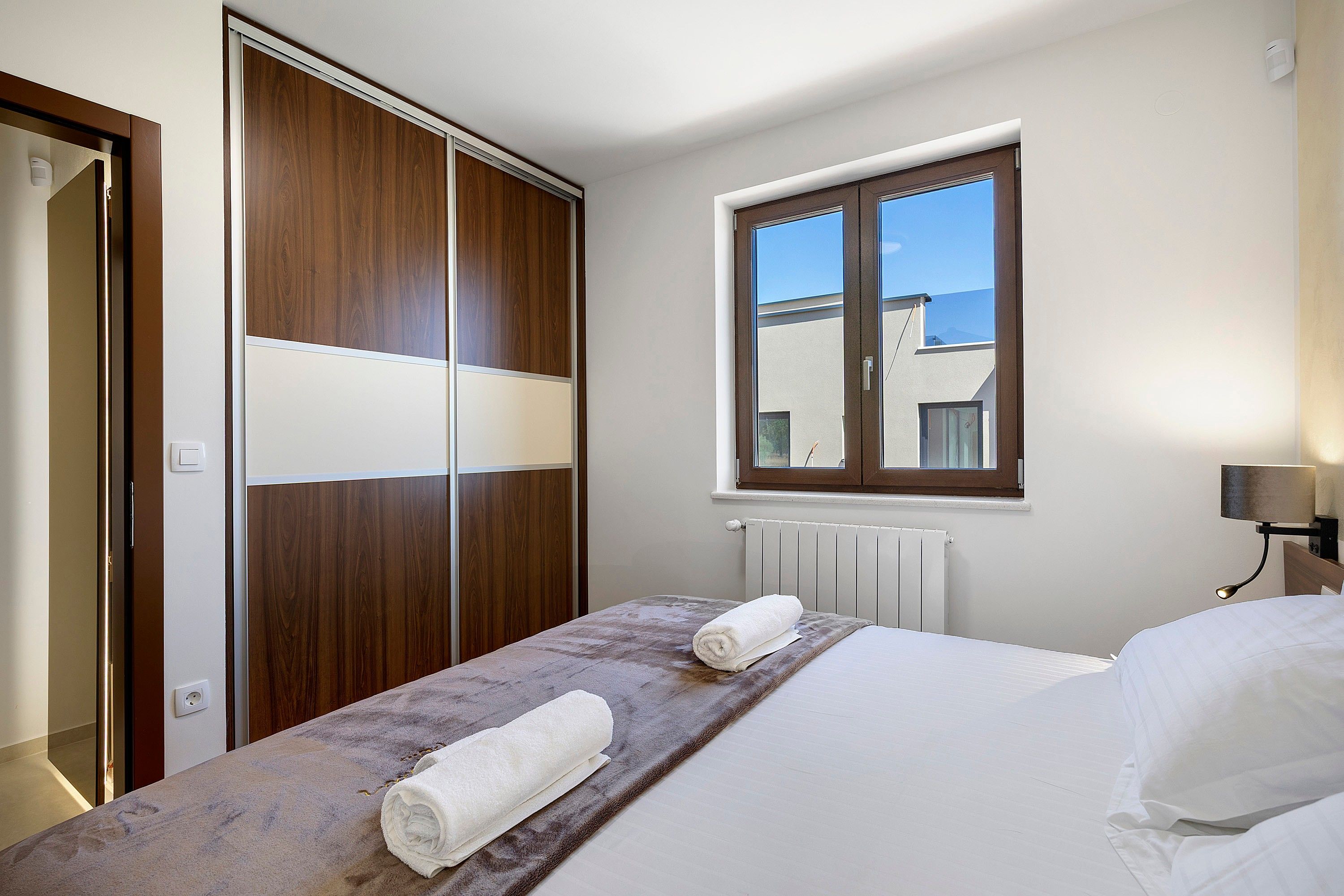 A hotel room with a bed, a window, a radiator, and a wardrobe.