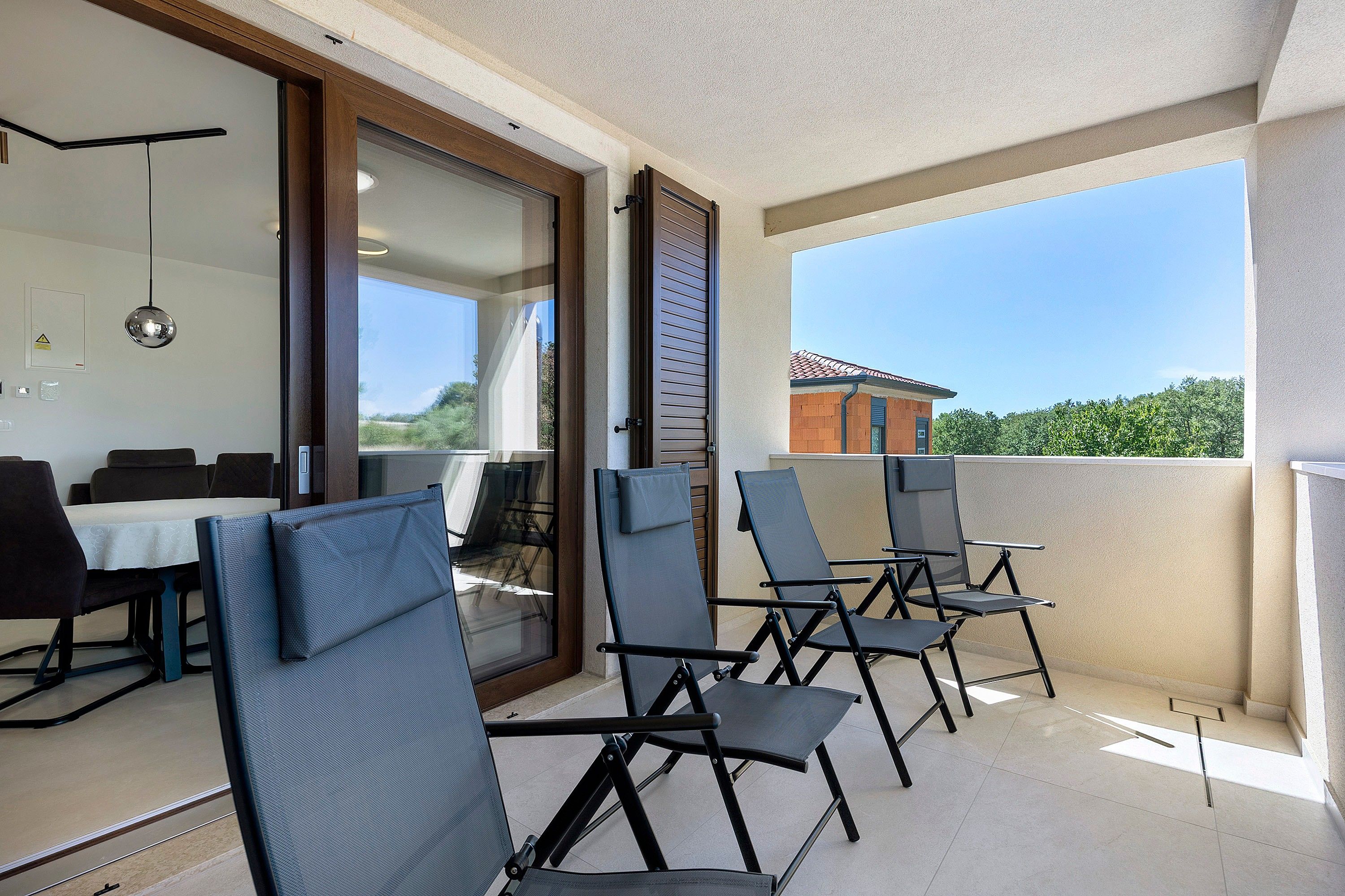 Een balkon buiten met een eethoek, inclusief stoelen en een tafel, en een uitzicht op een gebouw op de achtergrond.