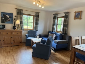 Ein Wohnzimmer mit einem Holzkabinett, einem blauen Sofa, einem blauen Sessel, einem kleinen Tisch mit einer Vase und einem Gemälde an der Wand.