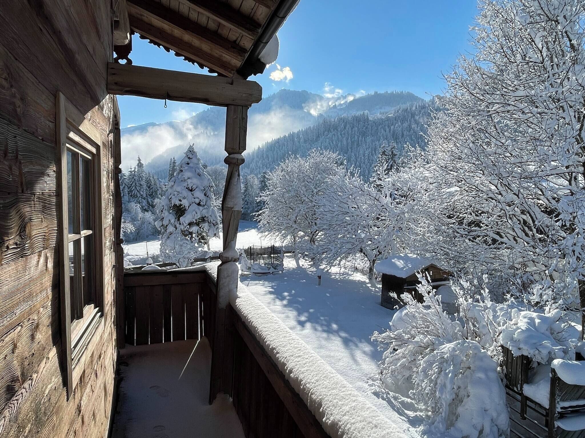 Una cabaña de madera con balcón que da a un paisaje nevado con árboles y montañas.