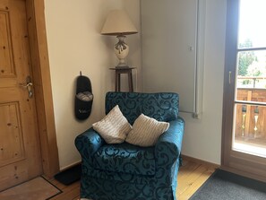 Ett rum med en blå soffa med mönster, en lampa, en dörr och en utsikt genom ett fönster.