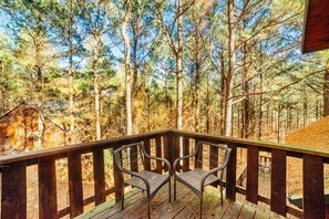 A wooden deck with two wicker chairs and a view of a forest. - Nestled in Nature: Pet-Friendly Family Cabin w/ Hot Tub, Arcade & Playground (Broken Bow)