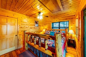 A wooden cabin bedroom with a bed, a window, and a door. - Nestled in Nature: Pet-Friendly Family Cabin w/ Hot Tub, Arcade & Playground (Broken Bow)