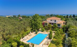 A large house with a swimming pool surrounded by greenery and a view of the sea.