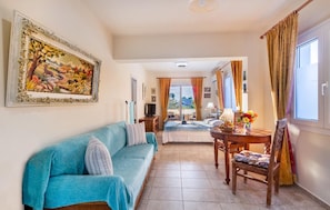 A living room with a sofa, a dining table with chairs, a TV, and a painting on the wall.