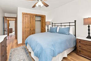 Une chambre à coucher comprenant un lit, des tables de chevet, une armoire et un ventilateur de plafond.