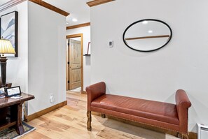 Une pièce avec un banc en bois, un miroir fixé au mur et une lampe sur une table.
