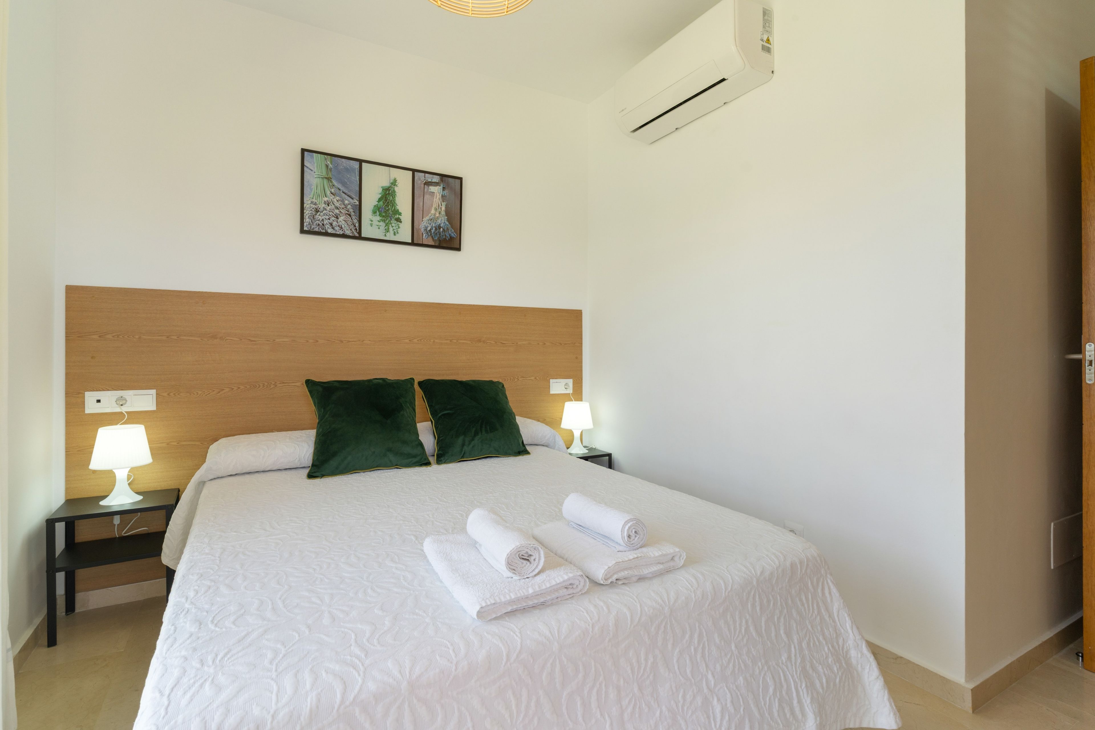 Een hotelkamer met een groot bed, twee bedlampen, een wandairconditioner en een ingelijst schilderij boven het bed.