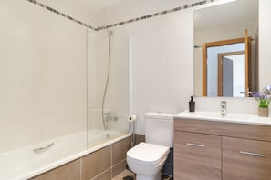 A bathroom with a bathtub, toilet, and vanity with a mirror.