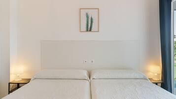 Een tweepersoonsbed met hoofdeinde, twee bedlampen, een stopcontact en een lijst met een cactusschilderij aan de muur.