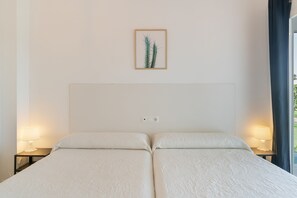 Una cama doble con cabecera, dos lámparas de noche, un enchufe y una obra de arte de un cactus enmarcado en la pared.
