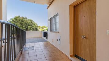 Ein Balkon mit Fliesenboden, Metallgeländer, einer Tür und einem Fenster mit Gitterstäben.