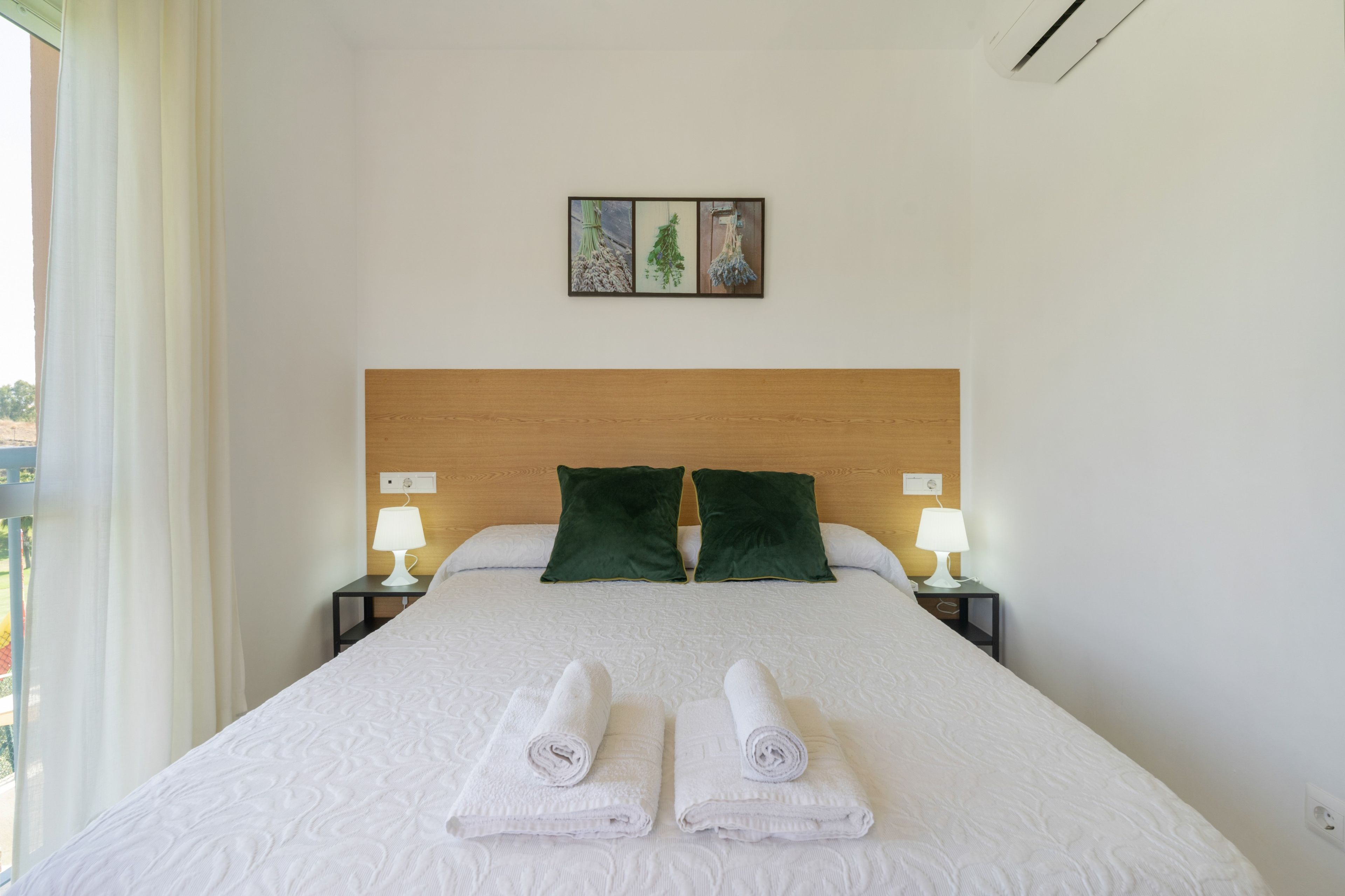 Ein Hotelzimmer mit einem großen Bett, zwei grünen Kissen, zwei Nachttischlampen und einem Gemälde an der Wand.