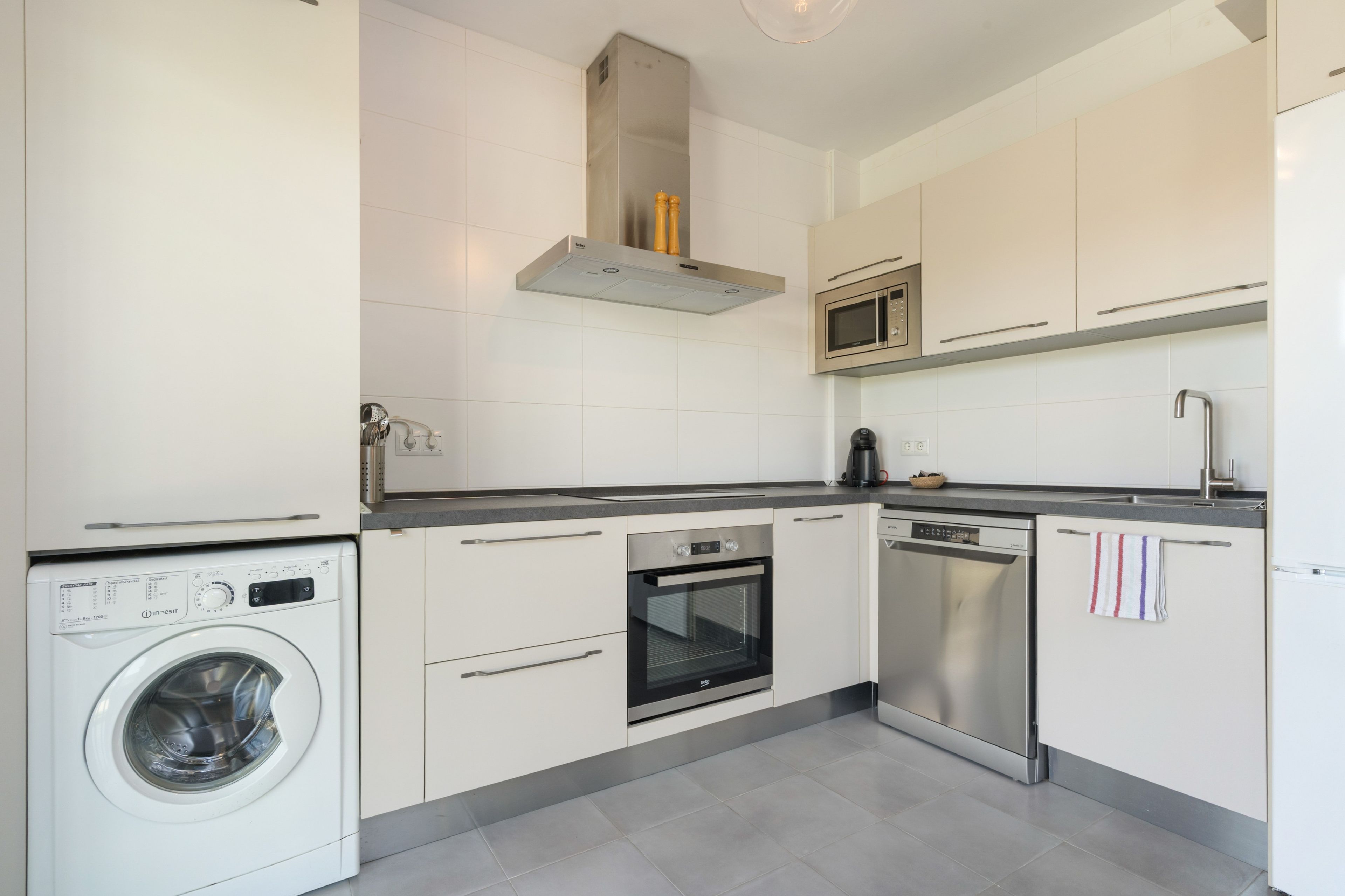 A modern kitchen with white cabinetry, a built-in washing machine, a microwave, an oven, and a dishwasher.