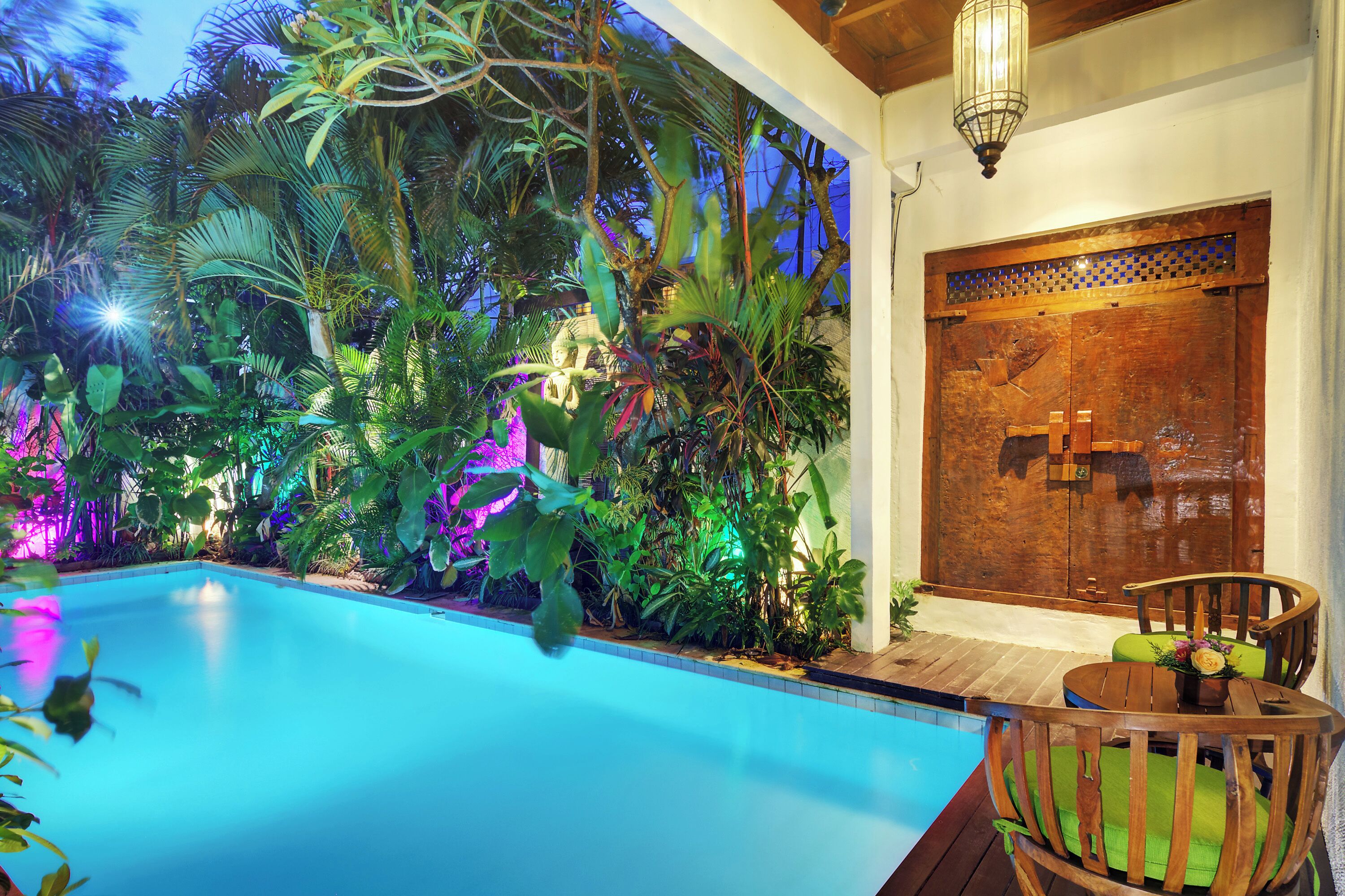 A swimming pool surrounded by lush tropical plants and a wooden door.