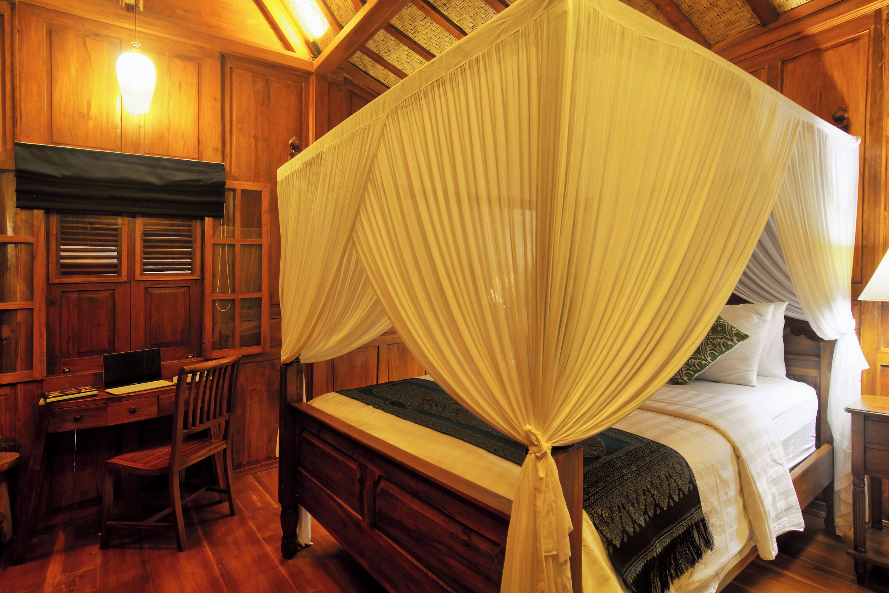 A wooden room with a four-poster bed, a desk, and a chair.