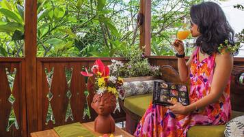 A woman sitting on a wooden bench with a table in front of her, holding a drink and a book titled 'Flavors of Indonesia'.