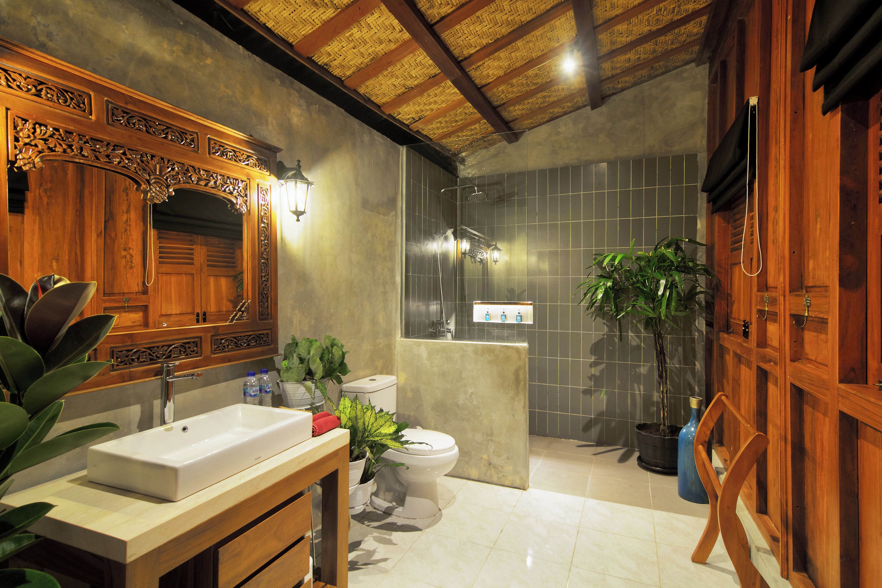 Une salle de bain avec un meuble-lavabo en bois, des toilettes, un espace douche et une plante en pot.