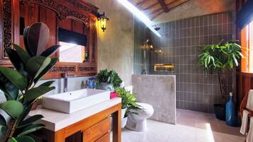 A bathroom with a wooden vanity, a white sink, a toilet, and a shower area.