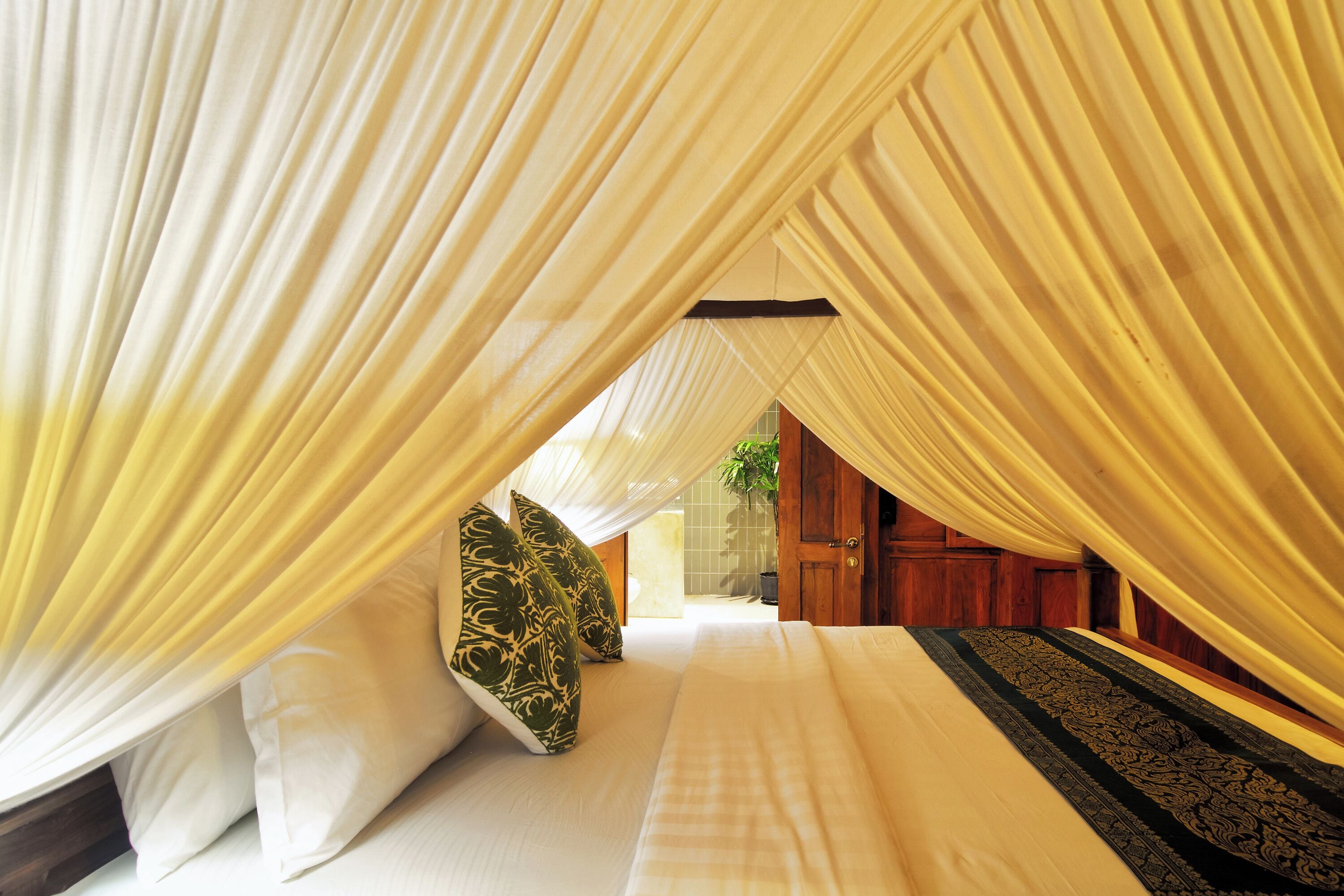 Una habitación con una cama, cortinas blancas y un tapete estampado.