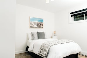 A bedroom with a bed, pillows, a bedside table with a lamp, a window, and a wall-mounted picture. - Le Doux Boisé - Beach Access - 15 min. from Mont Tremblant (LA CONCEPTION)