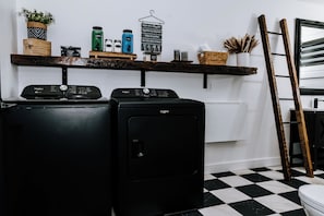 A laundry area with two Whirlpool washers, a shelf with various laundry supplies, and a checkered floor. - Le Doux Boisé - Beach Access - 15 min. from Mont Tremblant (LA CONCEPTION)
