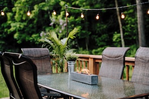 An outdoor dining area with a glass table, metal chairs, and a string of lights. - Le Doux Boisé - Beach Access - 15 min. from Mont Tremblant (LA CONCEPTION)