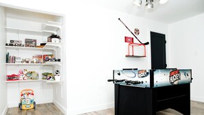 Ein Zimmer mit einem schwarzen Kicker, weißen Regalen mit diversen Gegenständen und einem Holzboden.