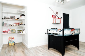 A room with a black foosball table, white shelves with various items, and a wooden floor. - Le Doux Boisé - Beach Access - 15 min. from Mont Tremblant (LA CONCEPTION)