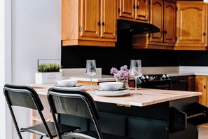A modern kitchen with wooden cabinets, a central island with seating, and a potted plant. - Le Doux Boisé - Beach Access - 15 min. from Mont Tremblant   (LA CONCEPTION)