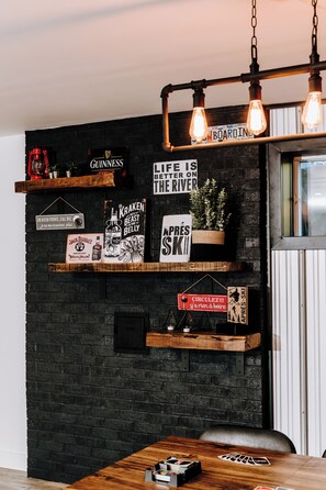 A room with a dark brick wall, wooden shelves displaying various signs and decorations, a hanging light fixture, and a window with blinds. - Le Doux Boisé - Beach Access - 15 min. from Mont Tremblant (LA CONCEPTION)