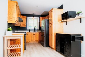 A kitchen with wooden cabinets, a black refrigerator, a microwave, and a dishwasher. - Le Doux Boisé - Beach Access - 15 min. from Mont Tremblant (LA CONCEPTION)