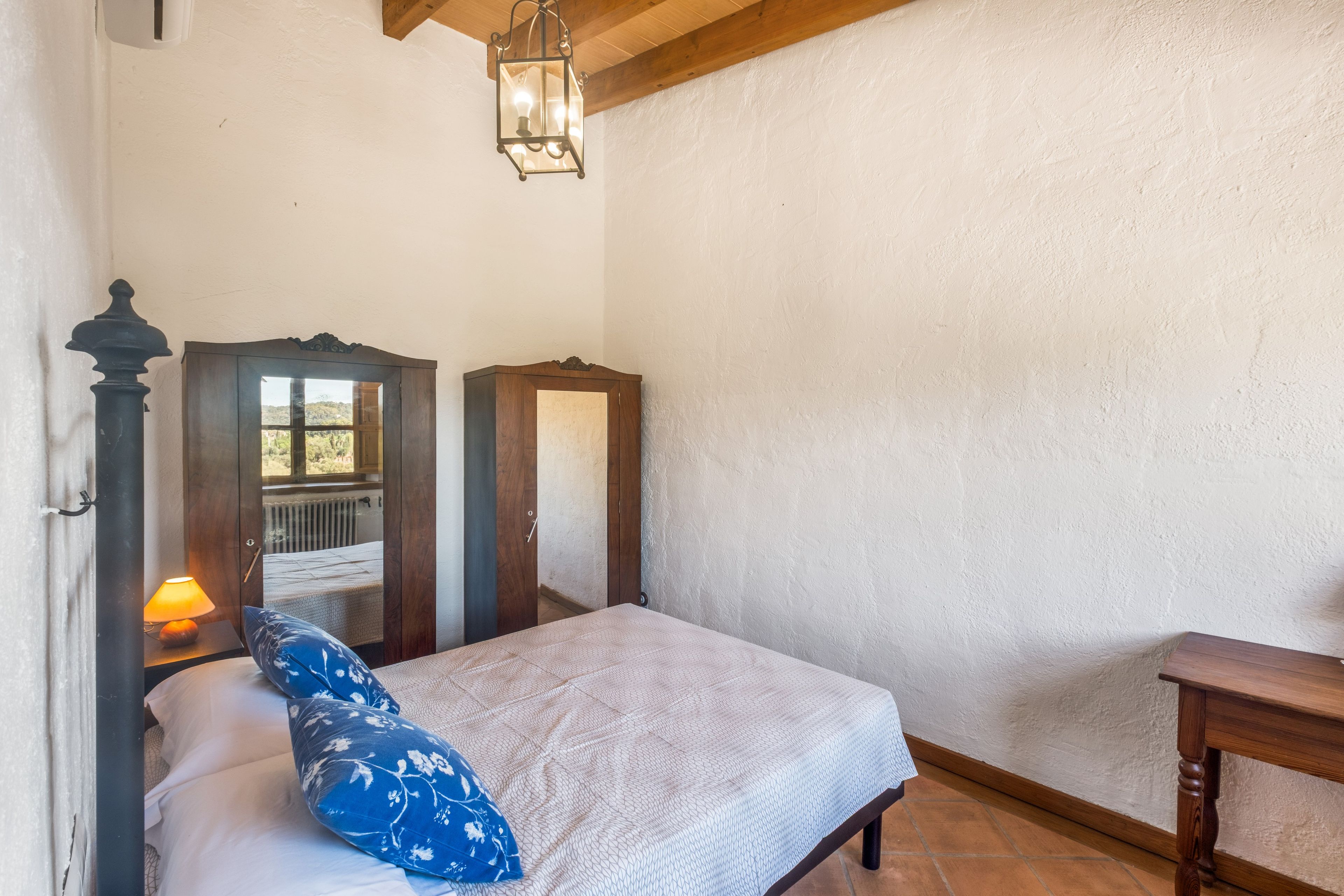 Ein Schlafzimmer mit einem Bett, einem Nachttisch mit Lampe, einem Holzschrank und einer Pendelleuchte.