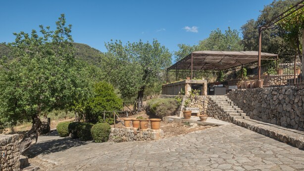 A stone pathway leading to a covered outdoor seating area with potted plants and a stone wall.