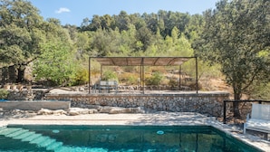 A swimming pool with a stone deck and a pergola with chairs.