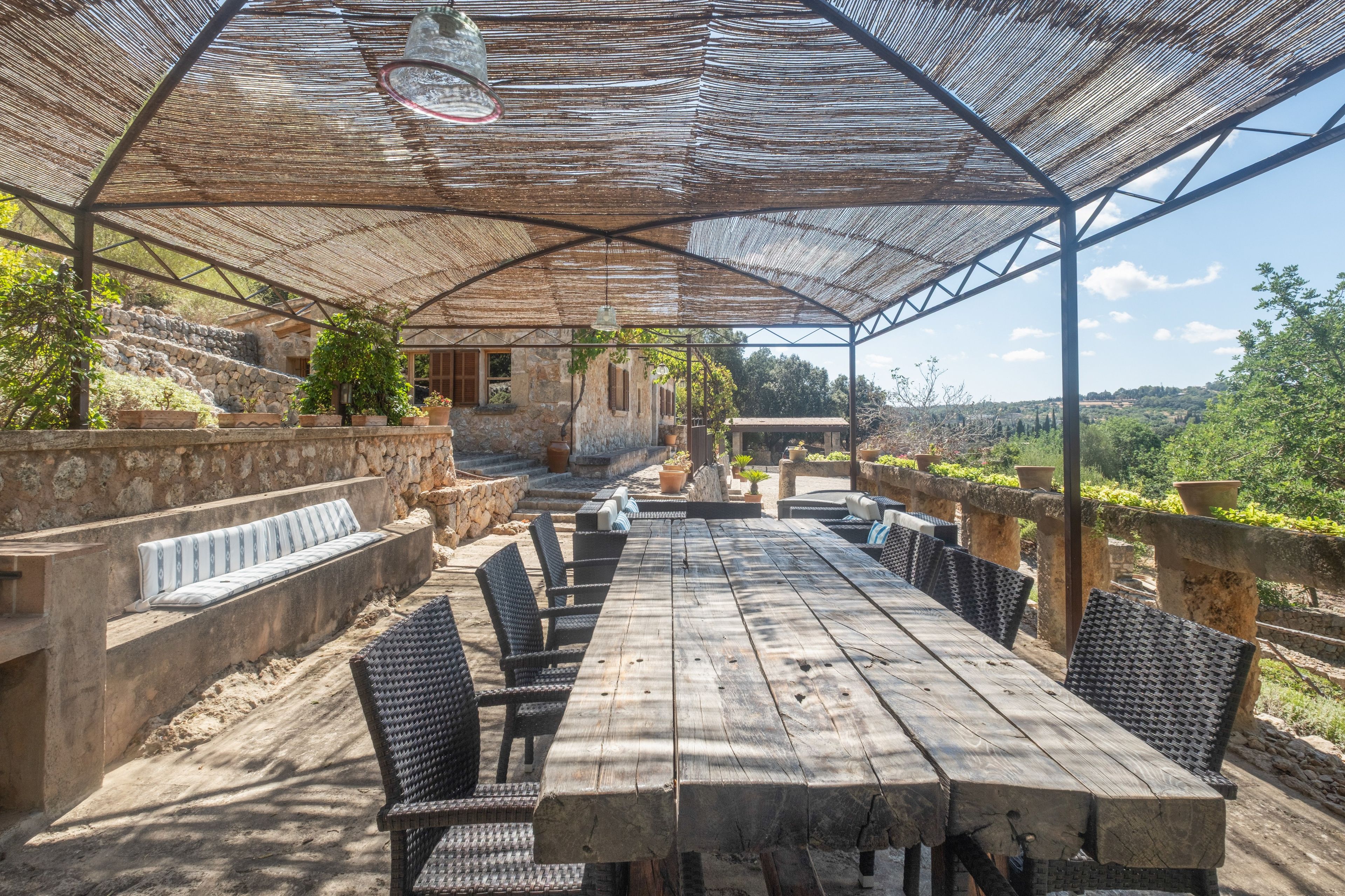 Un patio al aire libre con una mesa y sillas de madera, rodeado de muros de piedra y plantas en macetas.