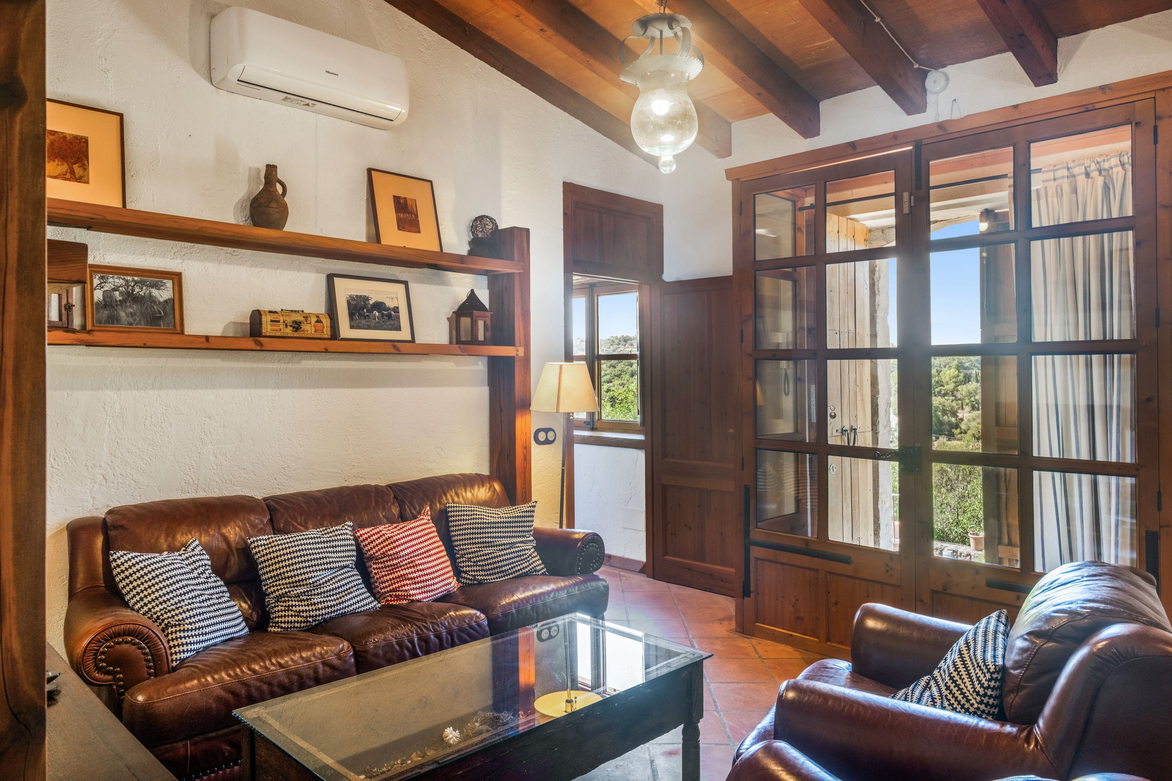 Una sala de estar acogedora con un sofá de cuero, una mesa de centro de vidrio, estantes de madera con adornos y un gran ventanal con cortinas.
